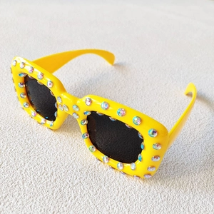 Close-up of square yellow sunglasses with colorful rhinestones on plastic frame