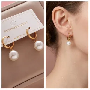 Detail of gold titanium steel hoop earrings with white pearls on a model and in a box