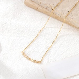 Gold smile necklace with curved baguette zircon pendant on a minimalist background