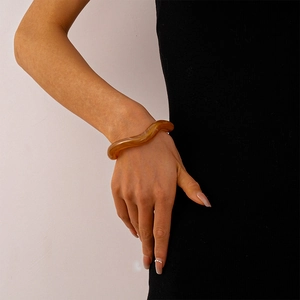 Detail of amber acrylic wavy bracelet featuring marbled resin texture on model's wrist