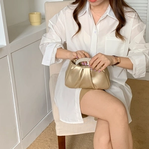 Golden pleated metallic clutch bag featuring a pearl handle displayed in a bright room