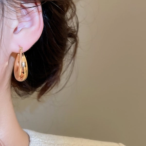 Détail de boucles d'oreilles goutte dorées avec finition miroir polie portées par mannequin