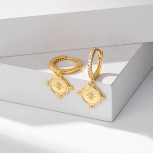 Detailed shot of gold hoop earrings with star engraved coin charms on white blocks