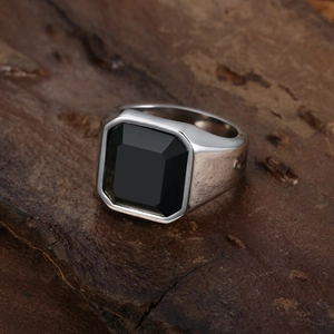 Close-up of men's silver ring with a square black gemstone on a rustic wooden surface