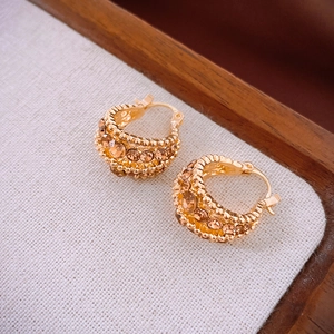 Close-up of golden C-shaped huggie earrings with amber crystals on white fabric