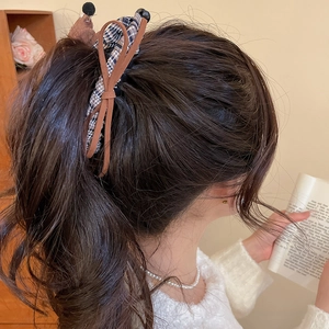 Detail showing oversized navy plaid bow hair clip worn by a model in a cozy indoor setting