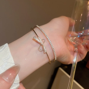 Detail of gold bow cuff and tennis bracelet set worn with elegant white lace sleeve