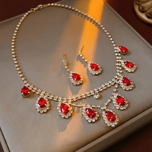 Elegant gold-tone jewelry set with red teardrop gems and crystals on a grey surface
