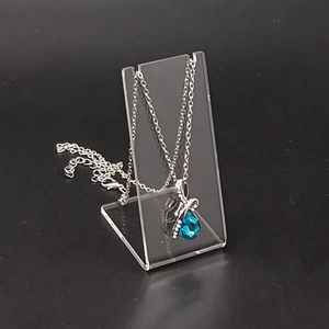 Detailed view of teardrop blue pendant necklace displayed on acrylic jewelry stand