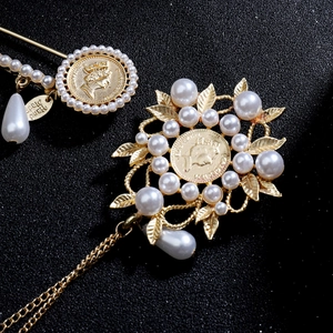 Macro detail of vintage gold brooch with pearl accents and carved coin pendant
