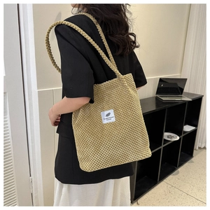 Detailed view of a beige corduroy tote bag with white fashion label on a model shoulder