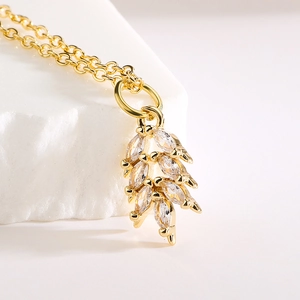 French style gold feather necklace with shimmering zircons on white textured stone