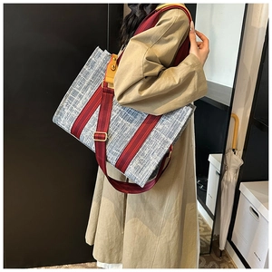 Detail of denim tote bag with red stripes, wide strap and leather accents on a model