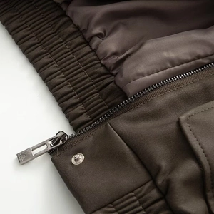 Detail of dark brown PU jacket featuring metallic zipper, snap button, and elastic hem