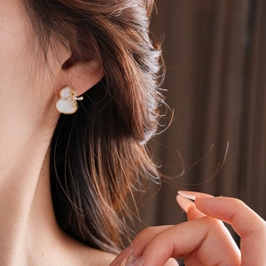 Detail view of gold-plated gourd stud earrings with mother of pearl and cross on a model