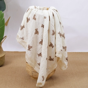 Detail of baby muslin blanket with brown bear print and tassel edges on woven basket