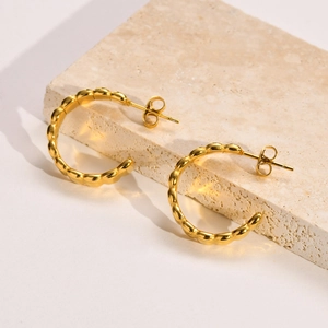 Detailed close-up of golden C-shaped hoop earrings with unique wavy beaded texture