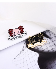 Close-up of pink and black axolotl enamel pins with I like you a lotl text banner