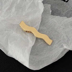 Close-up of golden wavy metal hair clip showing polished finish and spring mechanism