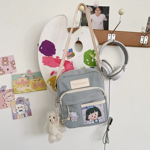 Sac bandoulière en toile grise avec écusson cartoon et breloque ours sur un mur