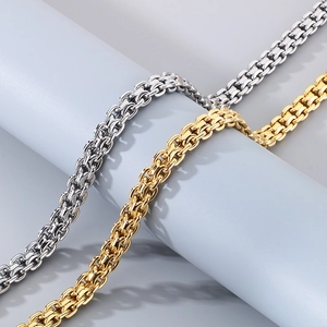 Close-up of gold and silver flat curb chain necklaces on a textured gray pedestal