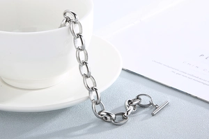 Silver steel chain bracelet with classic OT toggle closure draped on a white ceramic cup