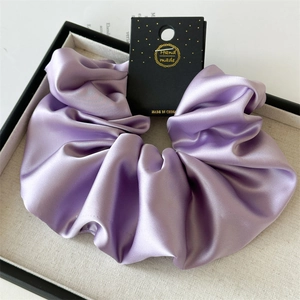 Detailed view of a purple oversized satin scrunchie with handmade tag on a display tray