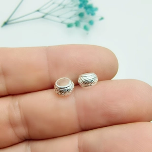 Macro view of silver alloy spacer beads with detailed feather texture and leaf carving