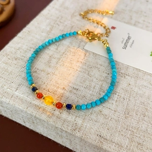 Détail d'un bracelet en perles colorées avec fermoir doré sur support en lin