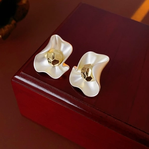Macro detail of gold and silver tone wavy stud earrings on a dark wooden jewelry box