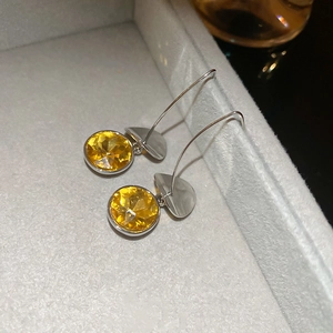 Macro detail of silver drop earrings with faceted round yellow citrine gemstones in a gray box