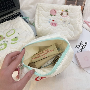 Close-up of cream quilted cosmetic bag with heart embroidery and colorful zipper detail