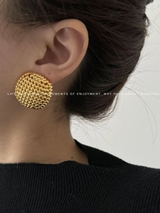 Close-up detail of oversized gold-toned round stud earring with fine beaded texture on model