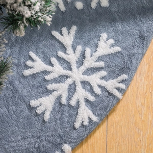 Gray plush Christmas tree skirt featuring a 3D white snowflake pattern on wooden floor