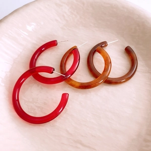 Detailed macro view of resin C-shape earrings in vibrant red and amber tortoise shell