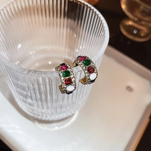 Close-up of golden C-shaped earrings with colorful gemstones and pavé crystals on glass
