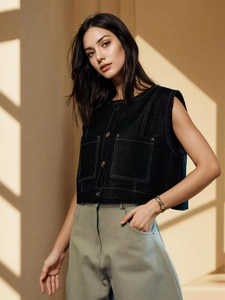 Detail of black denim vest and green wide-leg pants against modern artistic lighting shadows