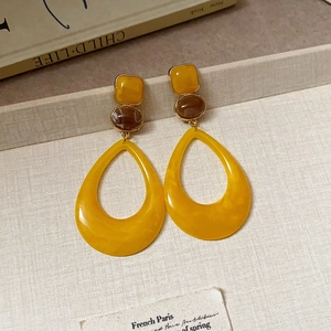 Close-up of yellow and brown geometric acrylic drop earrings with retro French style