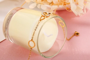 Detail of gold chain bracelet with rhinestone-inlaid ring and hollow round pendant