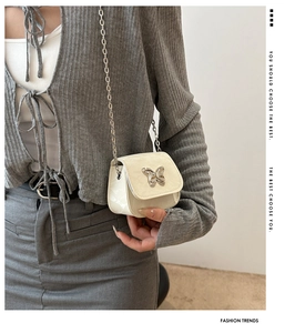 Close-up of white mini square bag with butterfly metal buckle and silver chain strap
