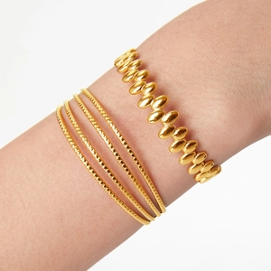 Golden titanium steel bangle set featuring geometric beads and oval links on a model