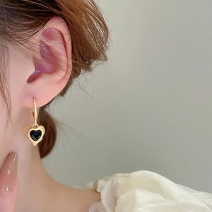 Close-up of elegant gold heart earrings with black enamel on a female model