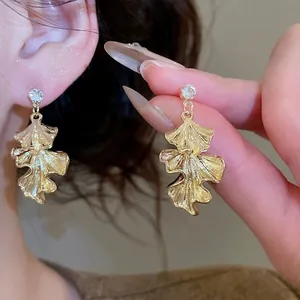 Golden ginkgo leaf dangle earrings with sparkling crystal studs on woman's ear