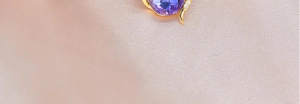 Macro shot of gold teardrop pendant with round purple gemstone and diamond accents