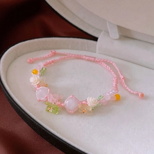 Close-up of a pink hand-woven bracelet with cat eye stones and white rose charms in a gift box