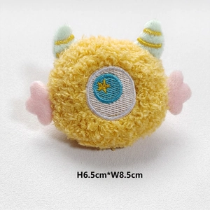 Detail view of yellow plush monster accessory with wings and dimensions H 6.5cm * W 8.5cm