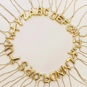 Flat lay of 26 3D balloon alphabet necklaces in polished gold stainless steel