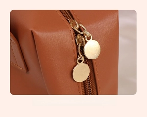Macro detail of the smooth dual gold metal zippers on the brown PU leather makeup bag