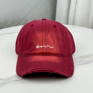 Close-up of wine red baseball cap featuring embroidered letters and distressed brim detail