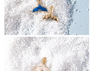 Macro detail of colorful enamel whale tail charms in blue gold and pink on white sand